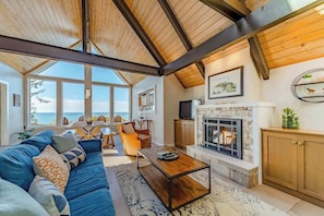 A spacious living room with a fireplace, a large sofa, and a view of the ocean. - Seagull's Bluff - Scenic Coastal Retreat with Ocean Views (Trinidad)