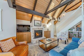 A spacious living area with a fireplace, a sofa, a coffee table, and a staircase leading to an upper level. - Seagull's Bluff - Scenic Coastal Retreat with Ocean Views (Trinidad)