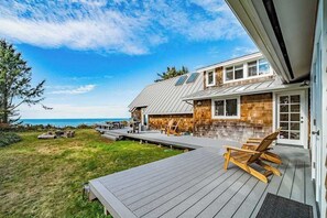 Een modern huis met een terras dat uitkijkt over een gazon en de oceaan.