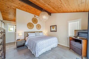 A bedroom with a wooden ceiling, a bed with a patterned bedspread, bedside lamps, and decorative wall art. - Seagull's Bluff - Scenic Coastal Retreat with Ocean Views (Trinidad)