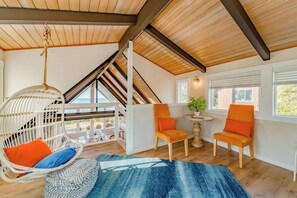 A room with a sloped ceiling, a hanging chair, two chairs, a small table, and a view through a window. - Seagull's Bluff - Scenic Coastal Retreat with Ocean Views (Trinidad)