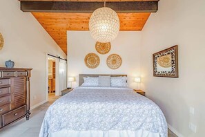 Een slaapkamer met een bed, nachtkastjes, een kaptafel, decoratieve wandkunst en een hanglamp.