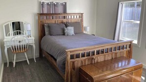 A bedroom with a wooden bed, a bedside table, a chair, and a window. - Cedar Street Cottage (Eureka)