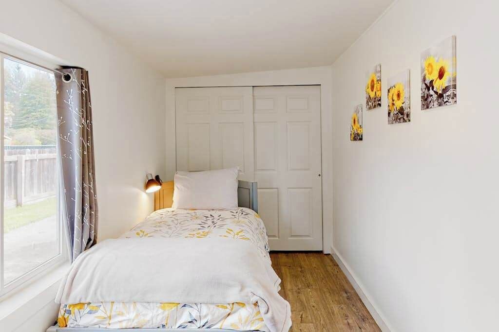 A bedroom with a bed, a wardrobe, a window with curtains, and wall art.