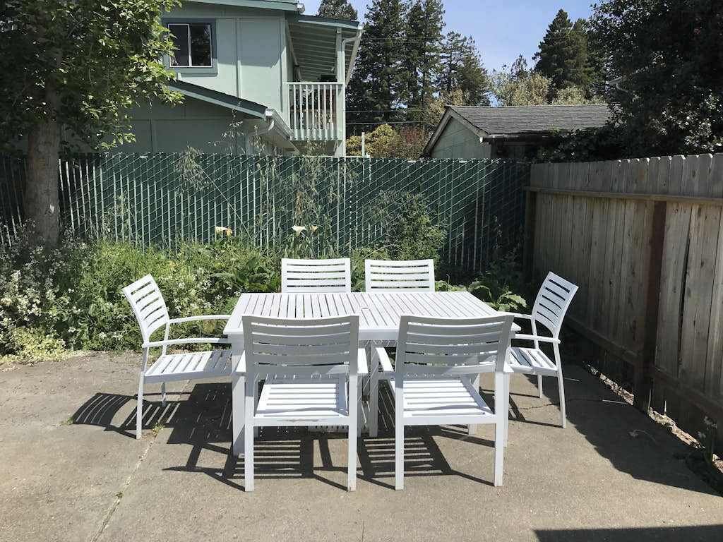An outdoor patio with a table and chairs, surrounded by a wooden fence and greenery.