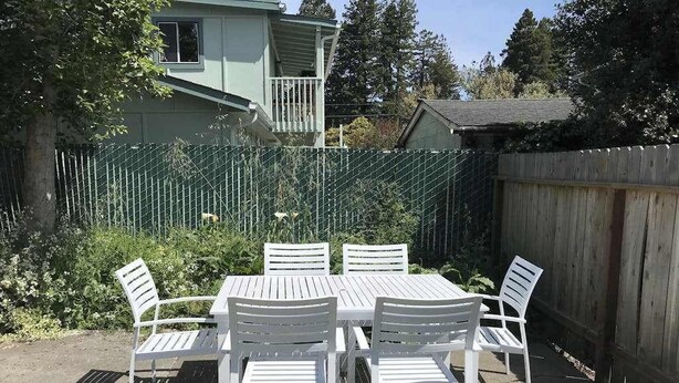 An outdoor patio with a table and chairs, surrounded by a wooden fence and greenery. - Cedar Street Cottage (Eureka)