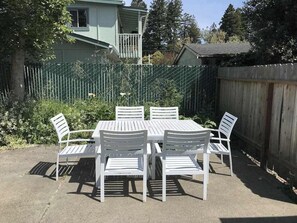 An outdoor patio with a table and chairs, surrounded by a wooden fence and greenery. - Cedar Street Cottage (Eureka)