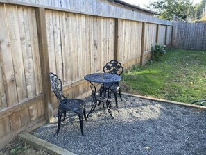 A patio with a wooden fence, a gravel surface, and a metal table and chairs. - Cedar Street Cottage (Eureka)