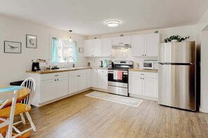 A modern kitchen with white cabinets, stainless steel appliances, and a wooden floor. - Cedar Street Cottage (Eureka)