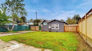 A residential backyard with a house, a wooden fence, and a green lawn. - Cedar Street Cottage (Eureka)