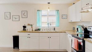 A kitchen with white cabinets, a granite countertop, a sink, a coffee maker, and a stove. - Cedar Street Cottage (Eureka)