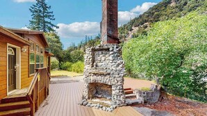 Eine Holzhütte mit Kamin aus Stein, einer Terrasse und einem Bergpanorama.