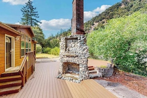 A wooden cabin with a stone fireplace, a deck, and a mountainous backdrop. - Trinity River Retreat (Willow Creek)