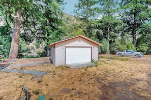 A small, single-story building with a garage door, surrounded by trees and a parked truck. - Trinity River Retreat (Willow Creek)