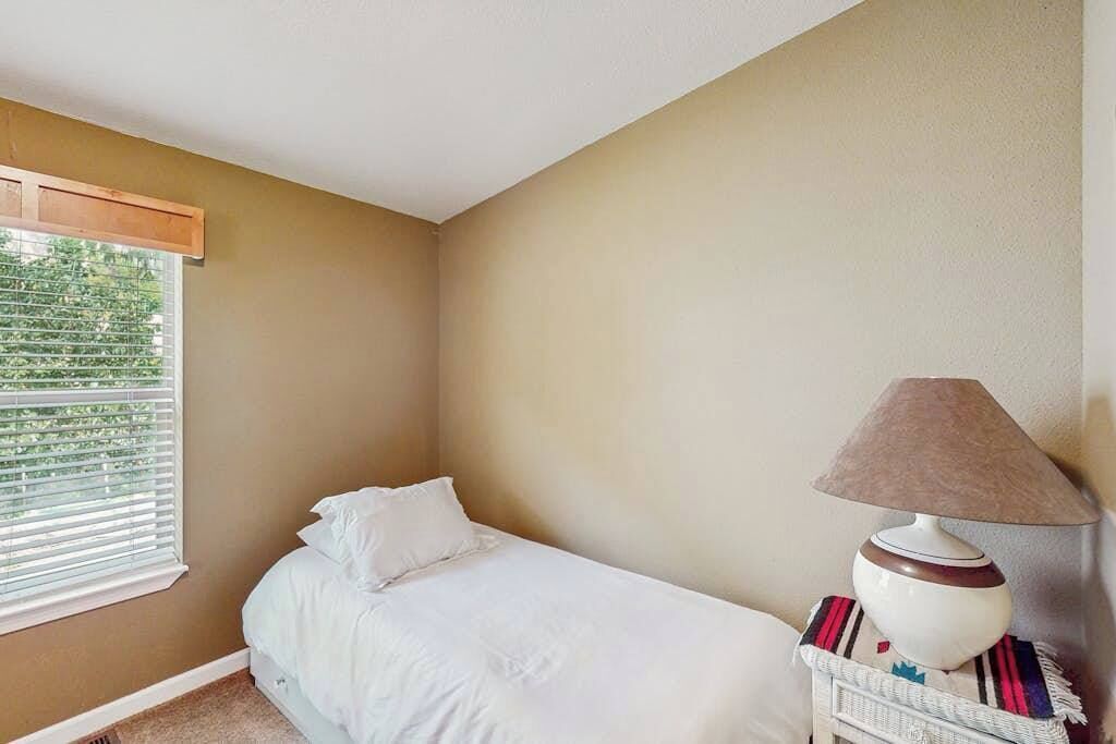 A bedroom with a bed, a window with blinds, and a lamp on a bedside table.