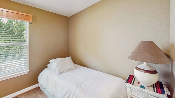 Ein Schlafzimmer mit einem Bett, einem Fenster mit Jalousien und einer Lampe auf einem Nachttisch.