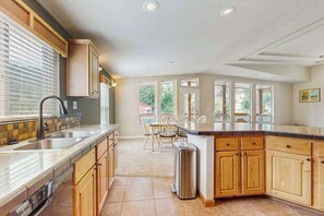 A kitchen with a central island, wooden cabinets, a stainless steel sink, and a dining area with chairs. - Trinity River Retreat (Willow Creek)