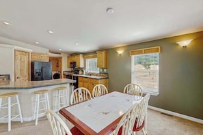 A kitchen with a central island, bar stools, and a dining table with chairs. - Trinity River Retreat (Willow Creek)