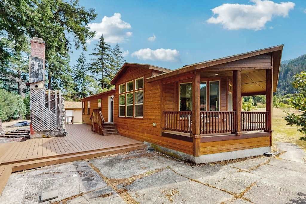 Une cabane en bois dotée d’une terrasse, de grandes fenêtres et d’une cheminée.