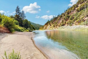 A riverbank with clear water, surrounded by greenery and trees. - Trinity River Retreat (Willow Creek)