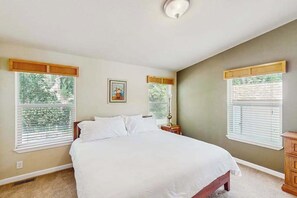A bedroom with a large bed, two windows with blinds, a nightstand, and a wall-mounted lamp. - Trinity River Retreat (Willow Creek)