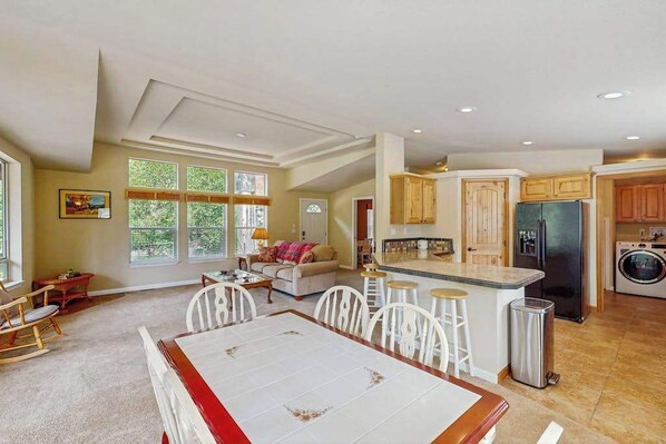 A spacious living area with a dining table, kitchen with wooden cabinets, and a large window providing natural light. - Trinity River Retreat (Willow Creek)