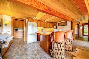 A wooden interior with a kitchen area, a bar counter, and seating. - La Casa Del Rio - Serene Riverside Getaway Surrounded by Nature (Salyer)