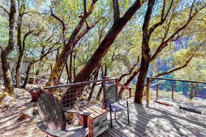 A wooden deck with a metal railing, surrounded by trees.