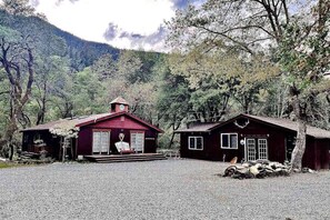 A rustic cabin with a red exterior, a porch, and a small adjacent building.