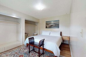 A bedroom with a bed, a chair, a nightstand, a painting on the wall, and a closet with a hanging rod. - Dean Getaway - Peaceful Coastal Escape for the Whole Family (Eureka)