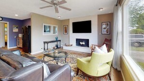 Ein Wohnzimmer mit Sofa, Sessel, Kamin, Fernseher und Deckenventilator.