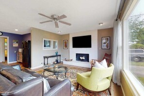 A living room with a sofa, armchair, fireplace, television, and a ceiling fan. - Dean Getaway - Peaceful Coastal Escape for the Whole Family (Eureka)
