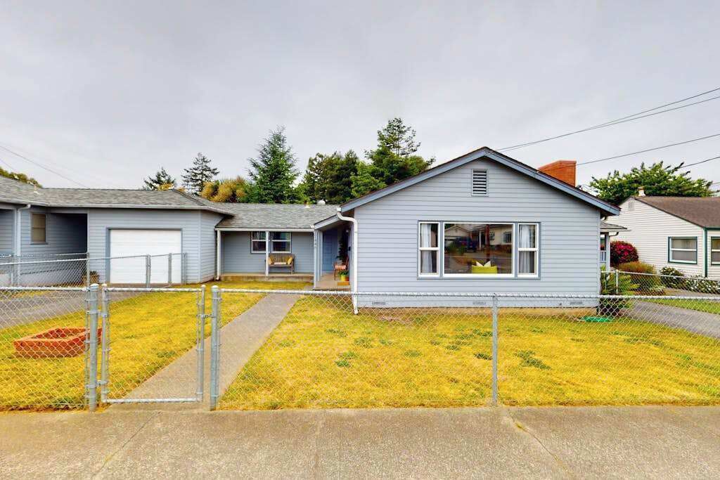 A residential property with a detached garage, a small house with a front porch, and a fenced yard.