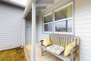 A wooden bench with cushions against a house wall, a window with blinds, and a concrete step leading to the porch. - Dean Getaway - Peaceful Coastal Escape for the Whole Family (Eureka)