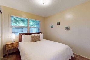 A bedroom with a bed, a nightstand, a window with blinds, and wall art. - Dean Getaway - Peaceful Coastal Escape for the Whole Family (Eureka)