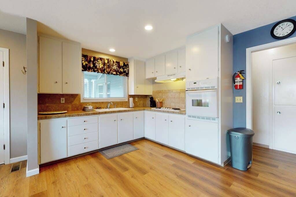 Una cocina moderna con armarios blancos, horno empotrado y una ventana con persianas.
