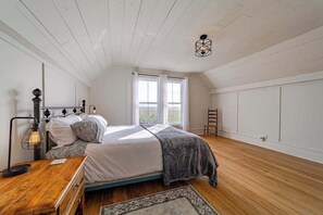 A bedroom with a bed, bedside table, lamp, and a view of the outdoors through a window. - 1858 Homestead - Historic Country Retreat with Modern Comforts (Ferndale)