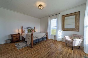 Een slaapkamer met een houten vloer, een bed met hoofdeinde, een nachtkastje, een stoel en een grote spiegel aan de muur.