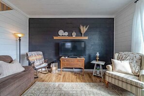 Un salon avec un mur de couleur sombre, un téléviseur posé sur un meuble en bois, un canapé marron, un fauteuil à rayures et un tapis à motifs.
