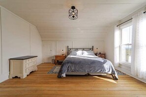 Une chambre à coucher avec un lit, des tables de chevet, un luminaire suspendu et une fenêtre avec des rideaux.