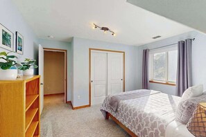 A bedroom with a bed, a wardrobe, a desk with a plant, and a window with curtains.