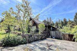 A rustic cabin with a stone wall, wooden deck, and a fenced yard.
