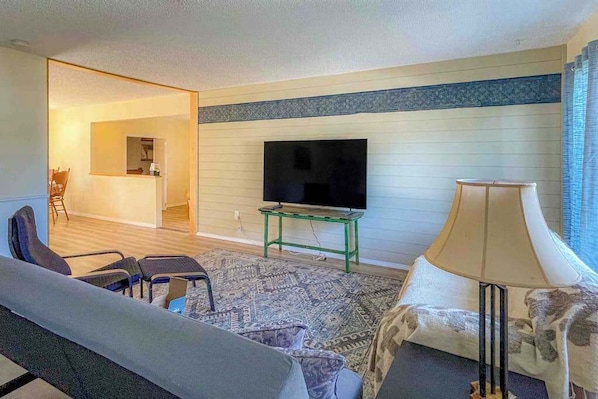 A living room with a sofa, chairs, a television on a stand, a lamp, and a patterned rug.