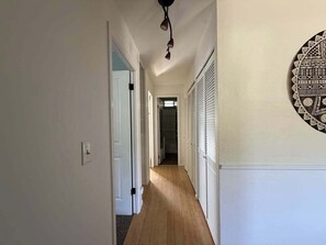 A hallway with a wooden floor, white walls, and a ceiling light fixture.