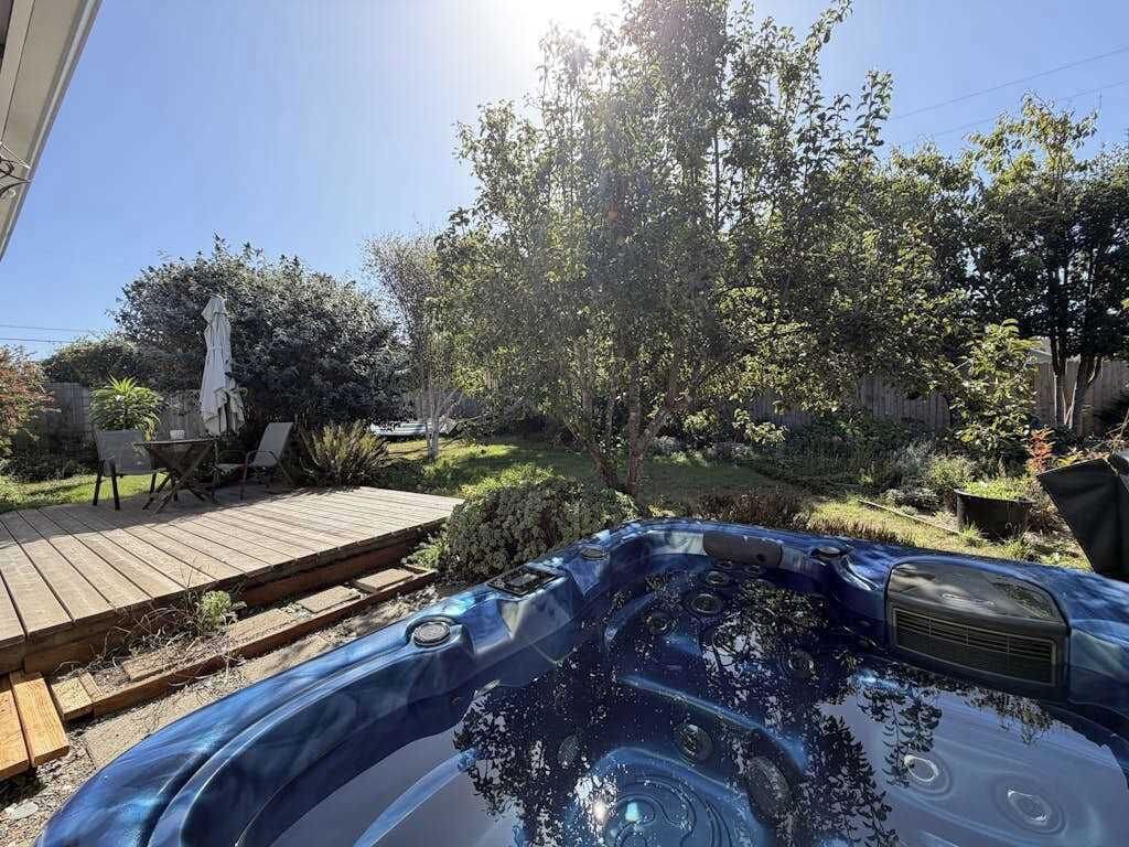 A hot tub in a backyard with a wooden deck, surrounded by trees and greenery.