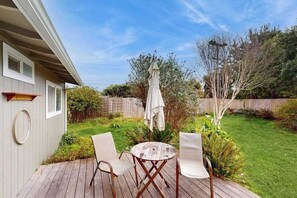 A deck with a round table and two chairs, surrounded by a wooden fence and greenery.