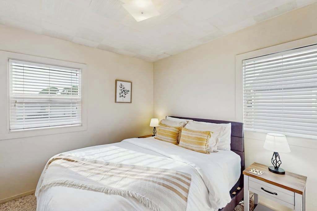 A bedroom with a bed, bedside table, lamp, and window blinds.