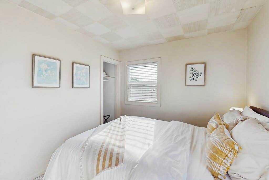 Een slaapkamer met een bed, een raam met jaloezieën en drie foto’s in lijsten aan de muur.