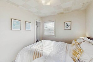 Une chambre à coucher avec un lit, une fenêtre avec des stores et trois tableaux encadrés accrochés au mur.