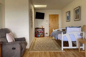 Ein Zimmer mit einem Bett, einem Schlafsofa, einem an der Wand befestigten Fernseher und einer Tür zu einem weiteren Raum.